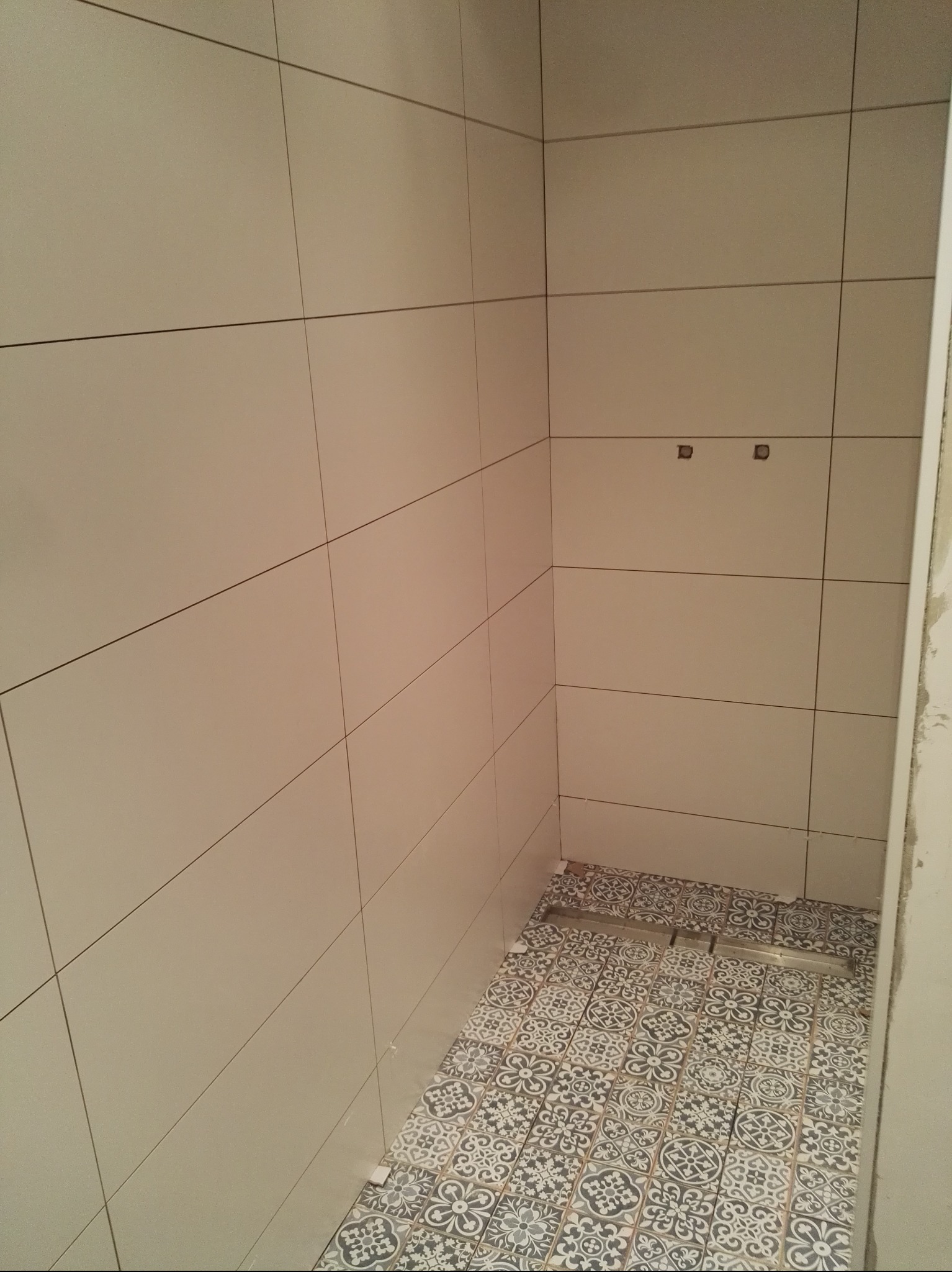 Wykończona kabina prysznicowa z beżowymi płytkami ściennymi i wzorzystą podłogą. Widoczny odpływ liniowy. Minimalistyczny design.