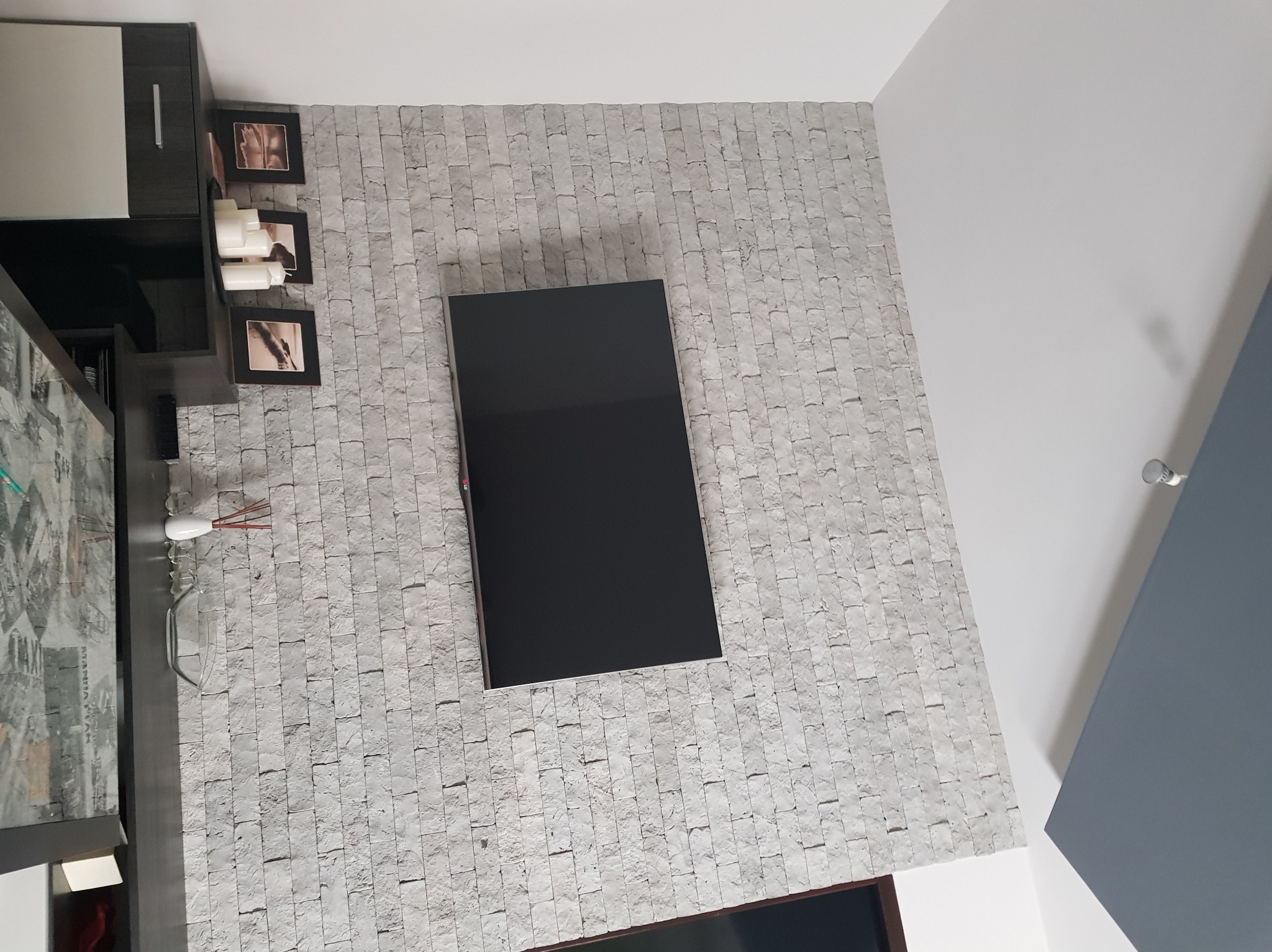 Ściana z dekoracyjnej cegły w salonie z zawieszonym telewizorem, obok szafka z dekoracjami i ramkami zdjęć. Nowoczesne wykończenie wnętrza.