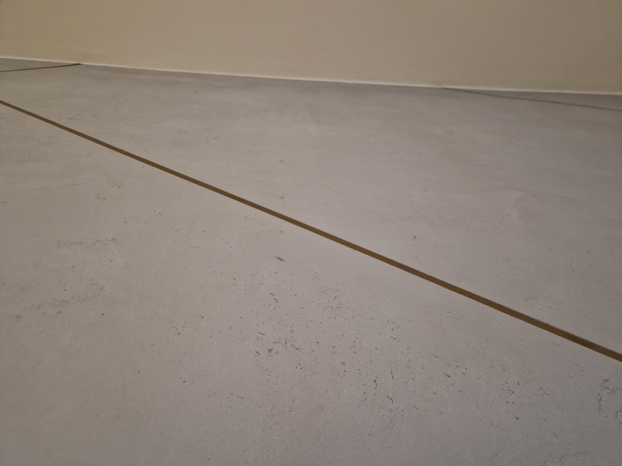 Szara, gładka posadzka z delikatną fugą w odcieniu brązu, przy ścianie w beżowym kolorze. Minimalistyczne wykończenie podłogi.
