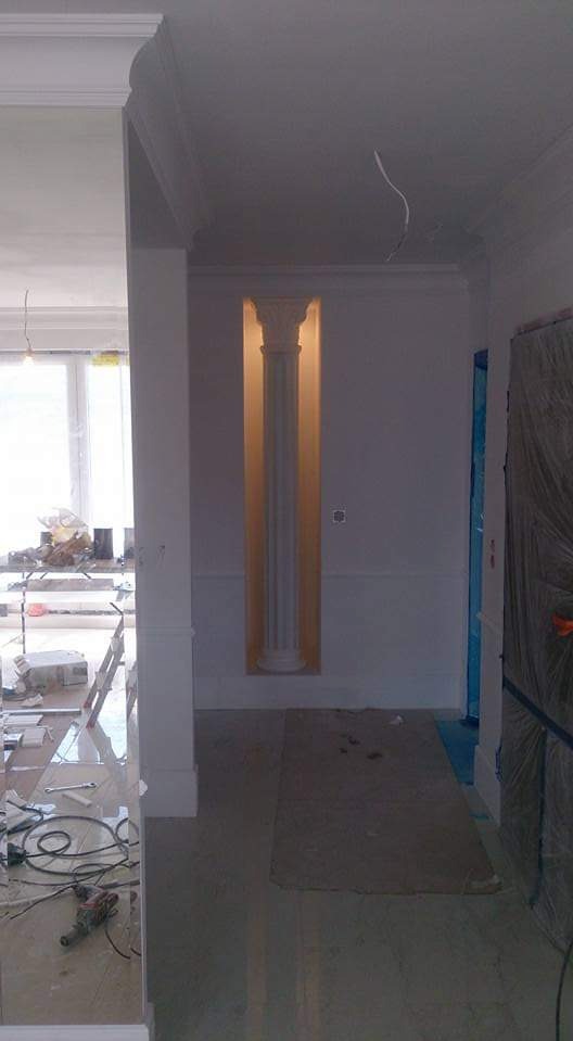 Wnęka z podświetloną kolumną dekoracyjną w trakcie prac wykończeniowych, widoczne kable i narzędzia na błyszczącej podłodze.