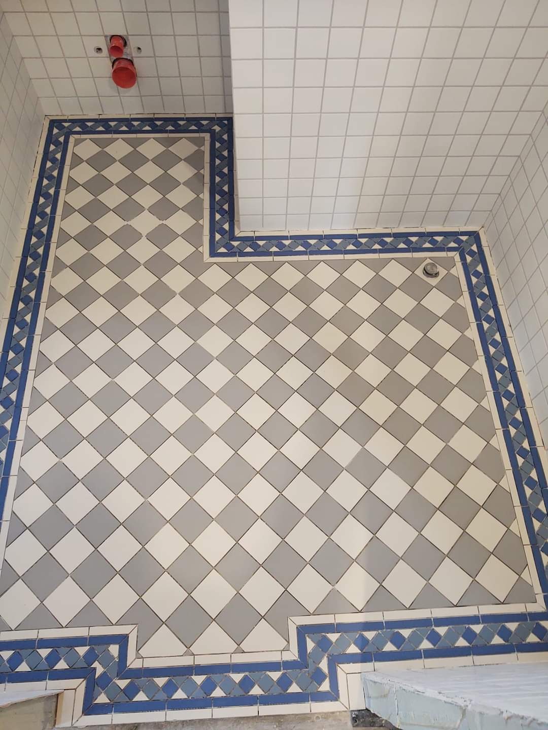 Ukończona podłoga w łazience w Skarszewach, z kwadratowymi płytkami ułożonymi w szachownicę w odcieniach szarości i bieli, z dekoracyjnym niebieskim obramowaniem.