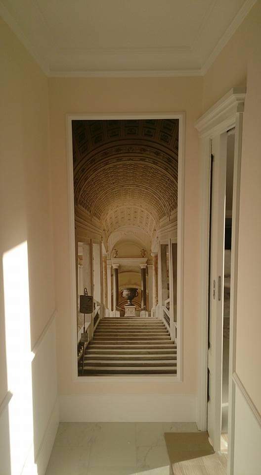 Korytarz z fototapetą przedstawiającą schody w monumentalnym wnętrzu z kolumnami i kopułą, wykończony w neutralnych odcieniach bieli i beżu.