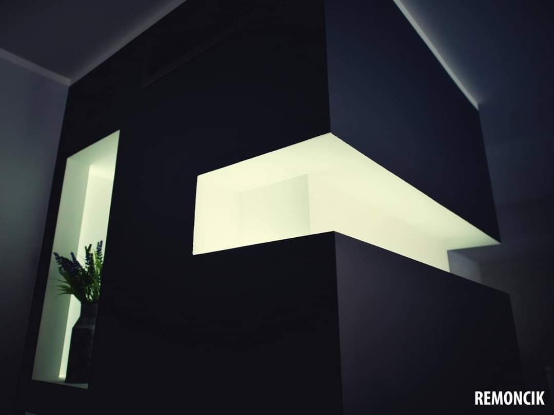 Nowoczesna ściana działowa z wnękami oświetlonymi od wewnątrz, czarna, matowa farba, w jednej wnęce wazon z lawendą.