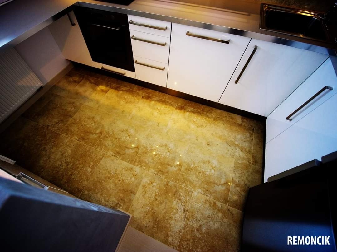 Ukończona aranżacja narożnej kuchni z białymi szafkami z podłużnymi uchwytami i podłogą wyłożoną brązowymi płytkami imitującymi kamień.