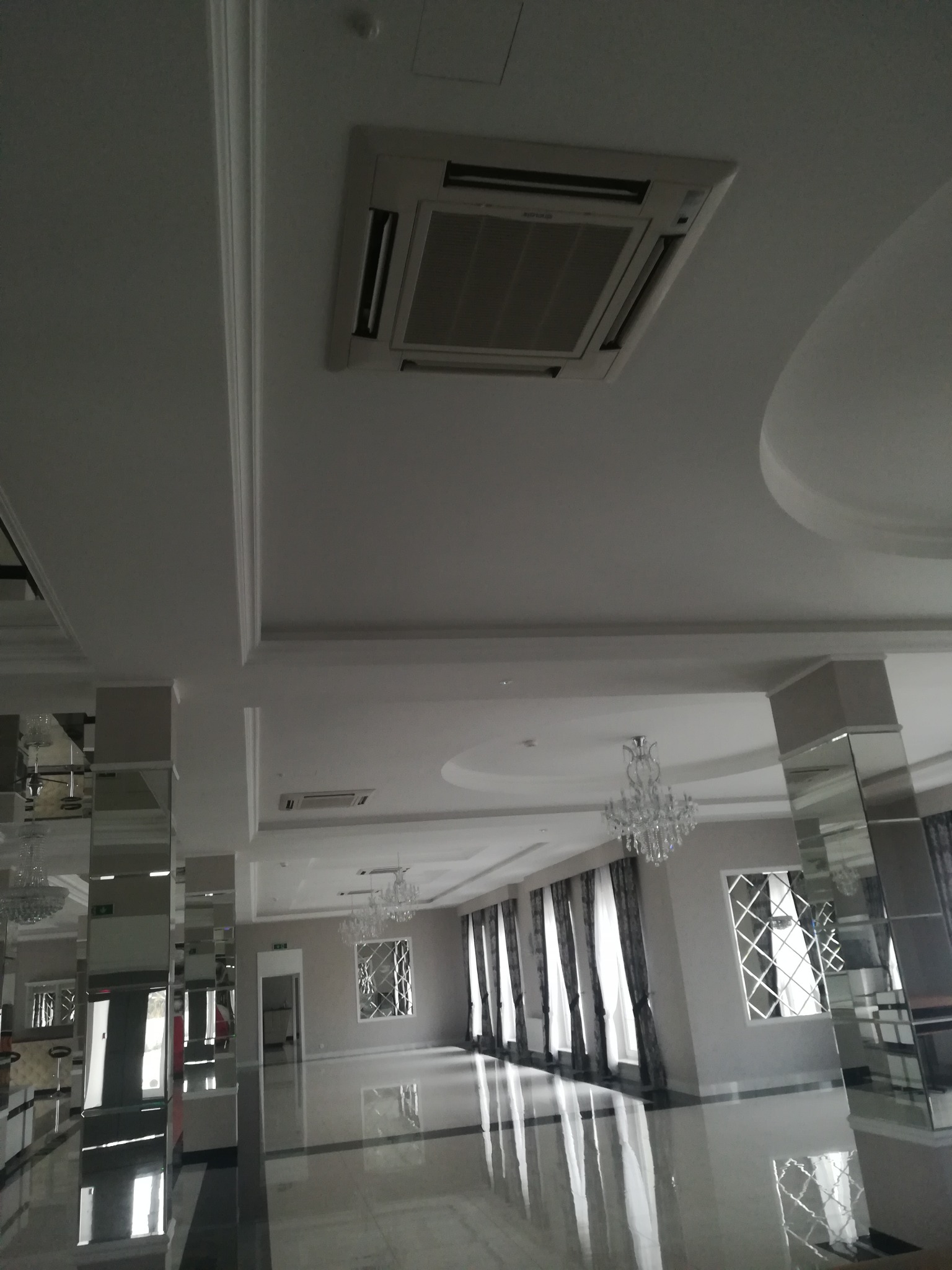 Kasetonowa klimatyzacja sufitowa w przestronnym, eleganckim wnętrzu sali balowej z lustrzanymi kolumnami i kryształowymi żyrandolami.