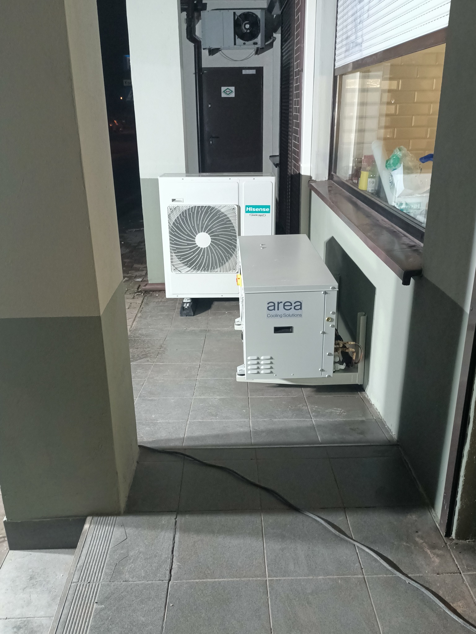 Zewnętrzne jednostki klimatyzacyjne Hisense i Area Cooling Solutions zainstalowane na szarych płytkach obok okna i drzwi.