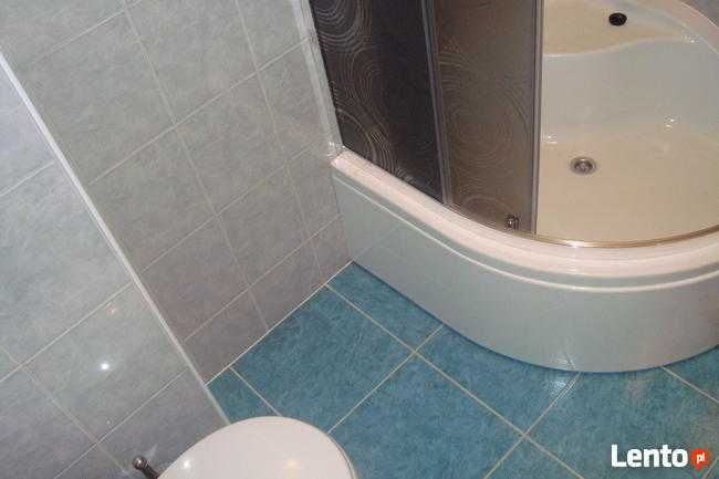 Wykończona łazienka z kabiną prysznicową i niebieskimi płytkami podłogowymi. Szare płytki ścienne. Ujęcie z góry, widoczny fragment toalety.