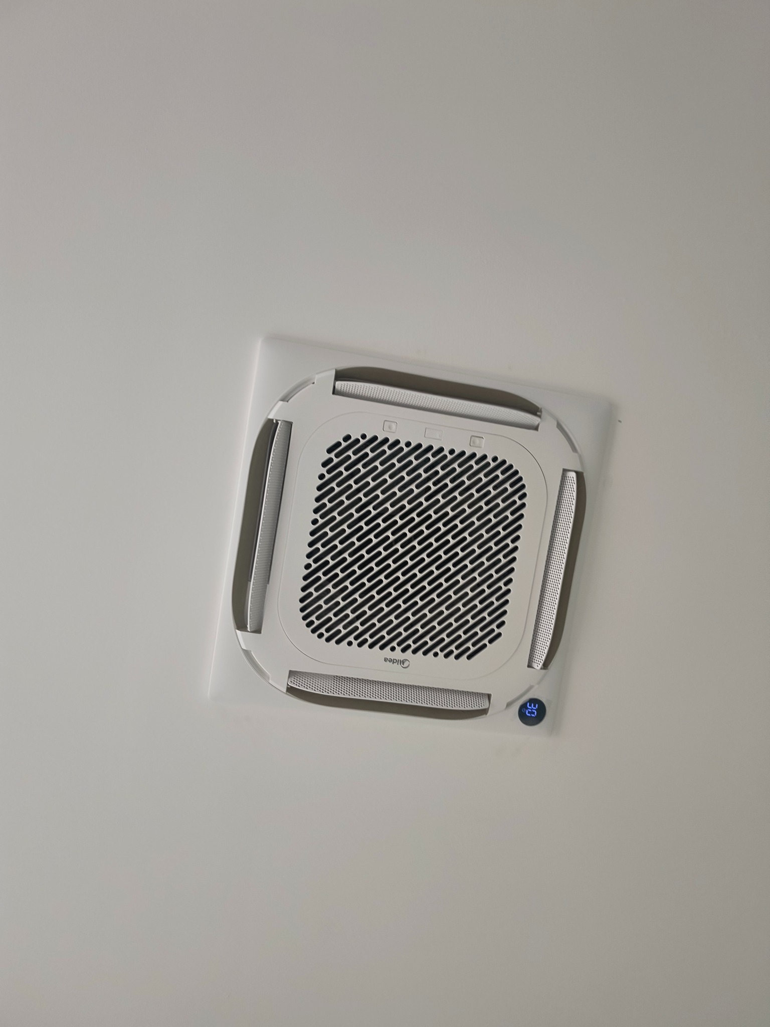 Kasetonowa klimatyzacja Midea zamontowana w suficie podwieszanym, widoczny wyświetlacz temperatury. Zdjęcie zrobione z dołu.