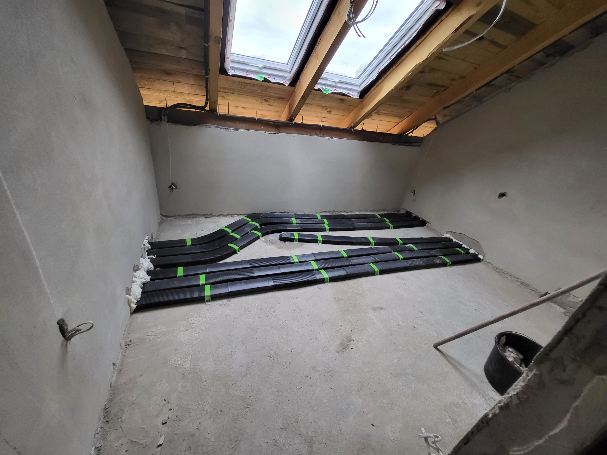 Czarny, karbowany przewód wentylacyjny ułożony na podłodze w surowym pomieszczeniu z oknem dachowym, zabezpieczony zieloną taśmą