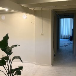 ADizajn - Wnętrze z białymi ścianami i podłogą, widok na korytarz z maszyną czyszczącą w tle, roślina doniczkowa na pierwszym planie