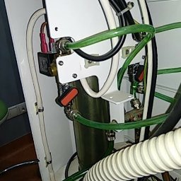 Zmywarka Plus 500 - Wnętrze pralki z widocznymi przewodami, zaworami i elementami elektrycznymi, w tym cewką z czerwonymi konektorami, oraz fragmentem zielonego węża doprowadzającego wodę.