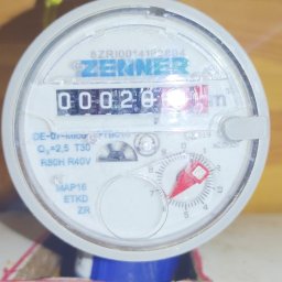 Zmywarka Plus 500 - Licznik wody Zenner z widocznym wskazaniem 0.0020 m3, zamontowany na rurze, z uszczelnieniem na gwincie i drewnianym tłem.