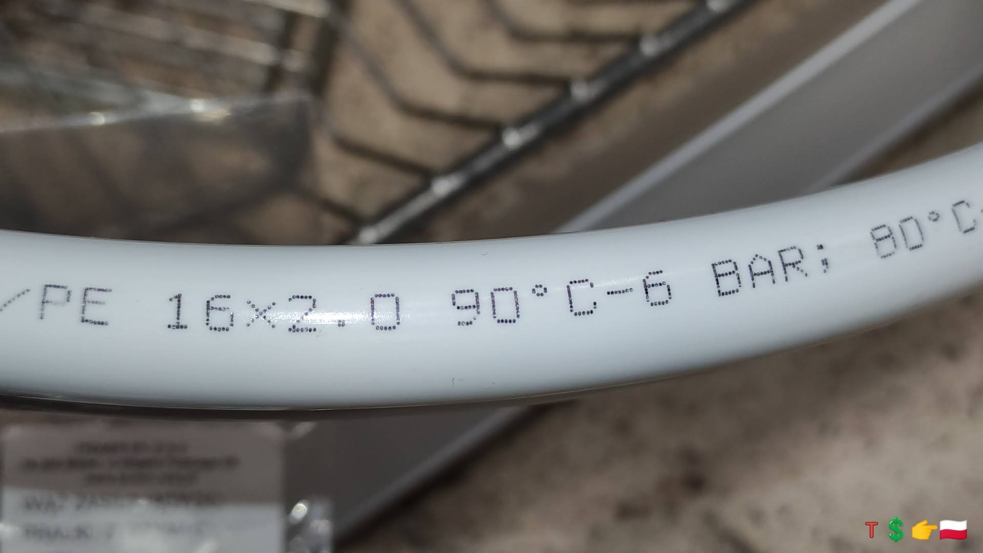 Biała rura PE 16x2.0 z nadrukowanymi specyfikacjami technicznymi: 90°C, 6 BAR, 80°C, widoczna na tle metalowej kraty.