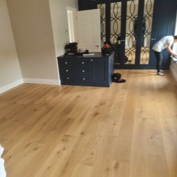 krzysztof - Jasna, dębowa podłoga w pokoju z granatową zabudową szafy z lustrami w ozdobnych ramach oraz komodą w tym samym kolorze; osoba czyści okno w tle.