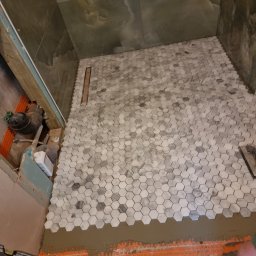 krzysztof - Układanie mozaiki heksagonalnej w szaro-białych odcieniach na podłodze prysznica, widoczny odpływ liniowy, poziomica i resztki zaprawy klejowej na pomarańczowej macie hydroizolacyjnej.