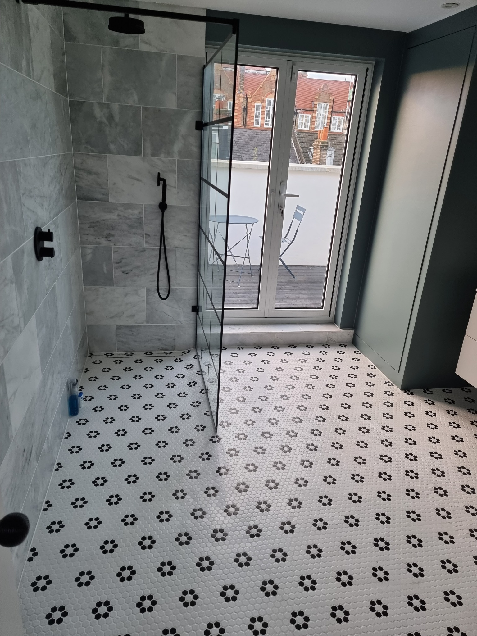 Nowoczesna łazienka w Opole Lubelskie z kabiną prysznicową typu walk-in, wykończona marmurowymi płytkami ściennymi i podłogą w biało-czarną mozaikę, z widokiem na balkon przez przeszklone drzwi.