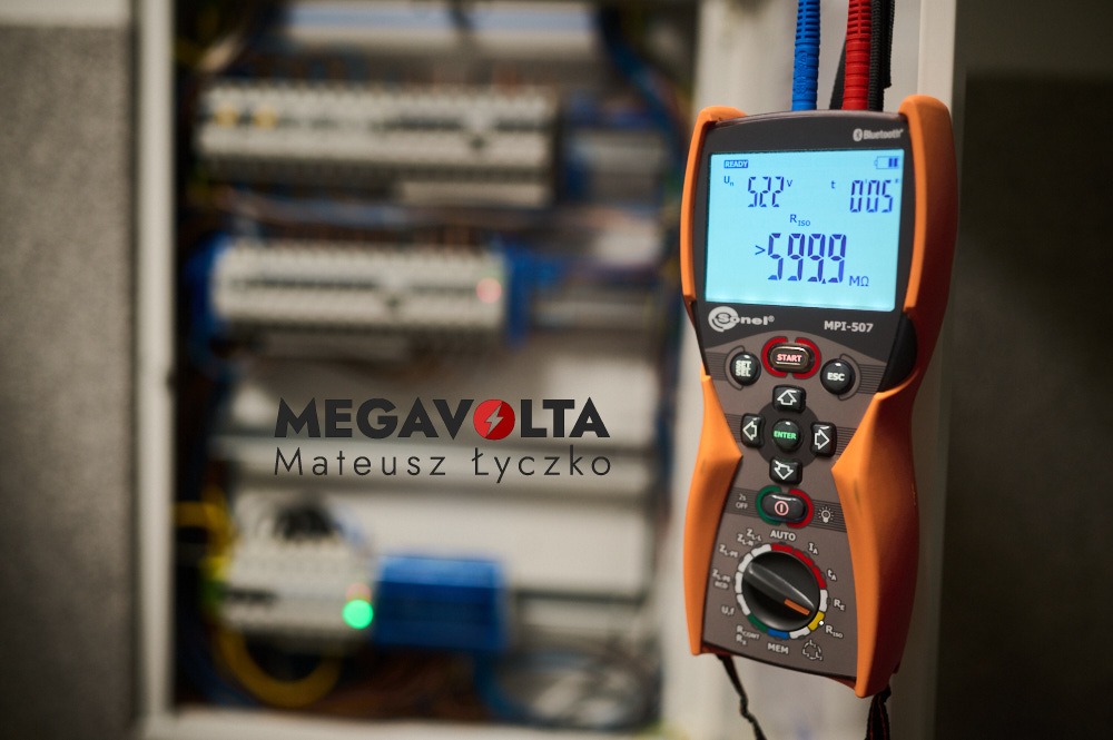 Miernik Sonel MPI-507 z wyświetlonym wynikiem pomiaru rezystancji izolacji na tle rozdzielnicy elektrycznej z widocznym logo firmy Megavolta.
