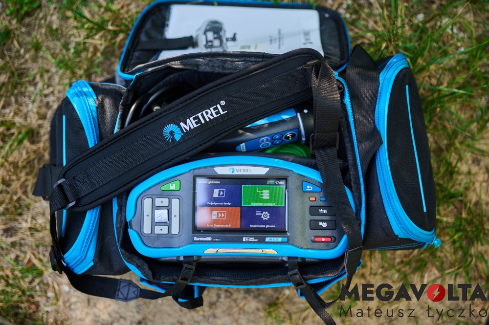 Otwarta torba narzędziowa firmy Metrel z widocznym miernikiem EurotestXD MN3315 oraz innymi akcesoriami na trawie.