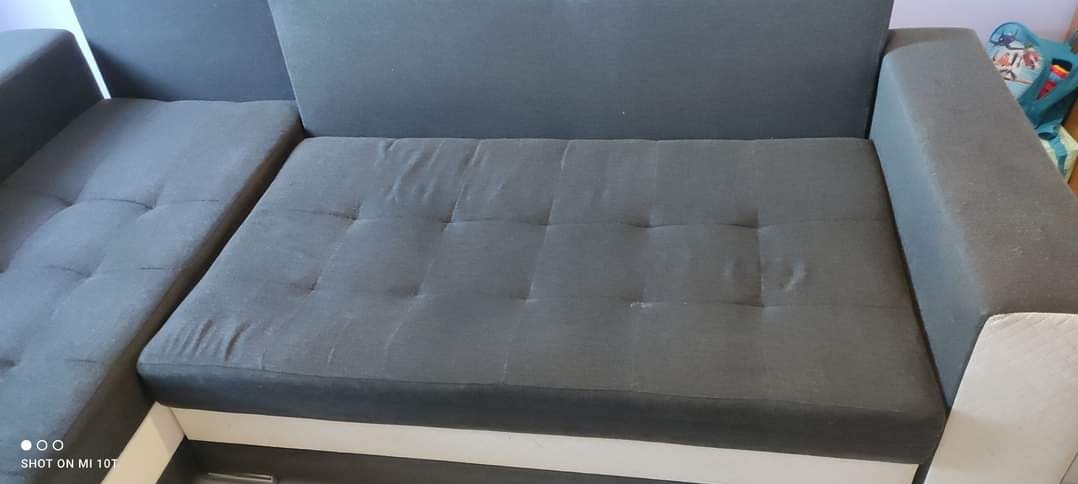 Szary narożnik z tapicerowanymi siedziskami z guzikami, widoczny z bliska, z elementami białej ramy.