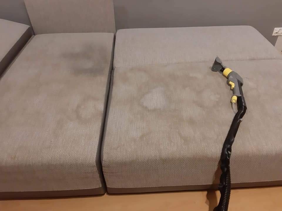 Beżowa sofa z widocznymi plamami czyszczona parownicą z szarą rączką i żółtymi detalami, ukazująca proces usuwania zabrudzeń.