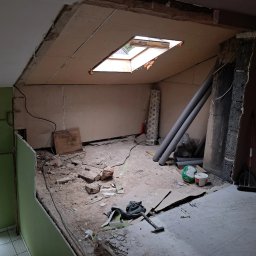 Wnętrze poddasza w trakcie demontażu: odsłonięte płyty kartonowo-gipsowe, gruz na podłodze, widoczne rury i narzędzia. Okno dachowe w suficie.