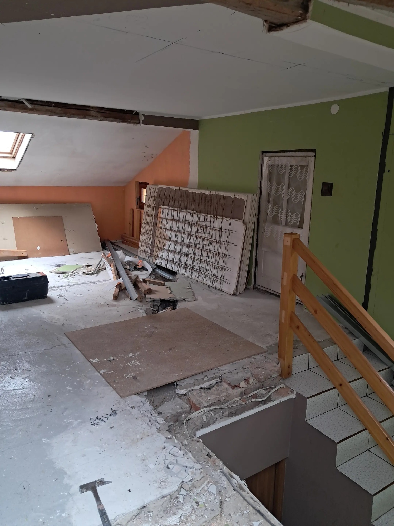 Wnętrze w trakcie przebudowy: odsłonięte belki stropowe, fragment schodów z drewnianą barierką, materiały budowlane i narzędzia. Widoczne ślady demontażu.