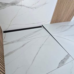 MJ BUD - Białe płytki podłogowe z marmurowym wzorem, ułożone z czarnymi fugami, sąsiadujące z drewnianą okładziną ściany z listew, oświetlone punktowym światłem.