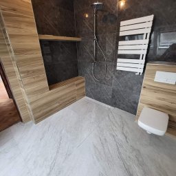 MJ BUD - Nowoczesna łazienka z szarymi marmurkowymi płytkami na ścianach i podłodze, deszczownicą, grzejnikiem drabinkowym i zabudową z drewnopodobnych paneli.