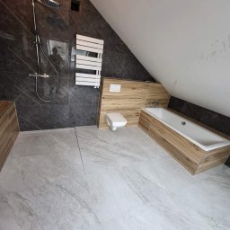 MJ BUD - Ukośna łazienka z szarymi płytkami imitującymi marmur na ścianie z prysznicem i białym grzejnikiem, drewnopodobnymi płytkami przy wannie i toalecie oraz jasnoszarą podłogą.