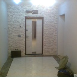 Sakhavat Samadov - Korytarz po remoncie z nową, jasną podłogą z płytek, ścianą wyłożoną tapetą imitującą cegłę i zamontowanymi drzwiami z matowego szkła.