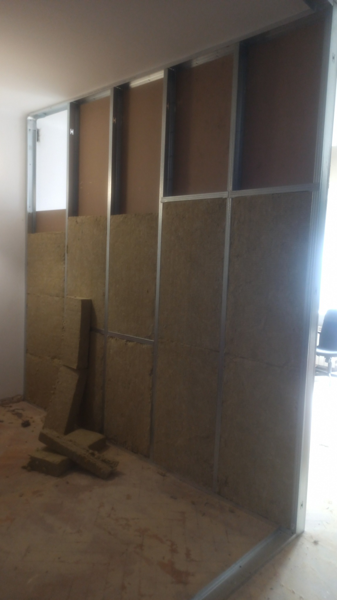 Konstrukcja ścianki działowej z profili metalowych wypełniona wełną mineralną, widoczne niedocięte fragmenty materiału izolacyjnego leżące na podłodze.