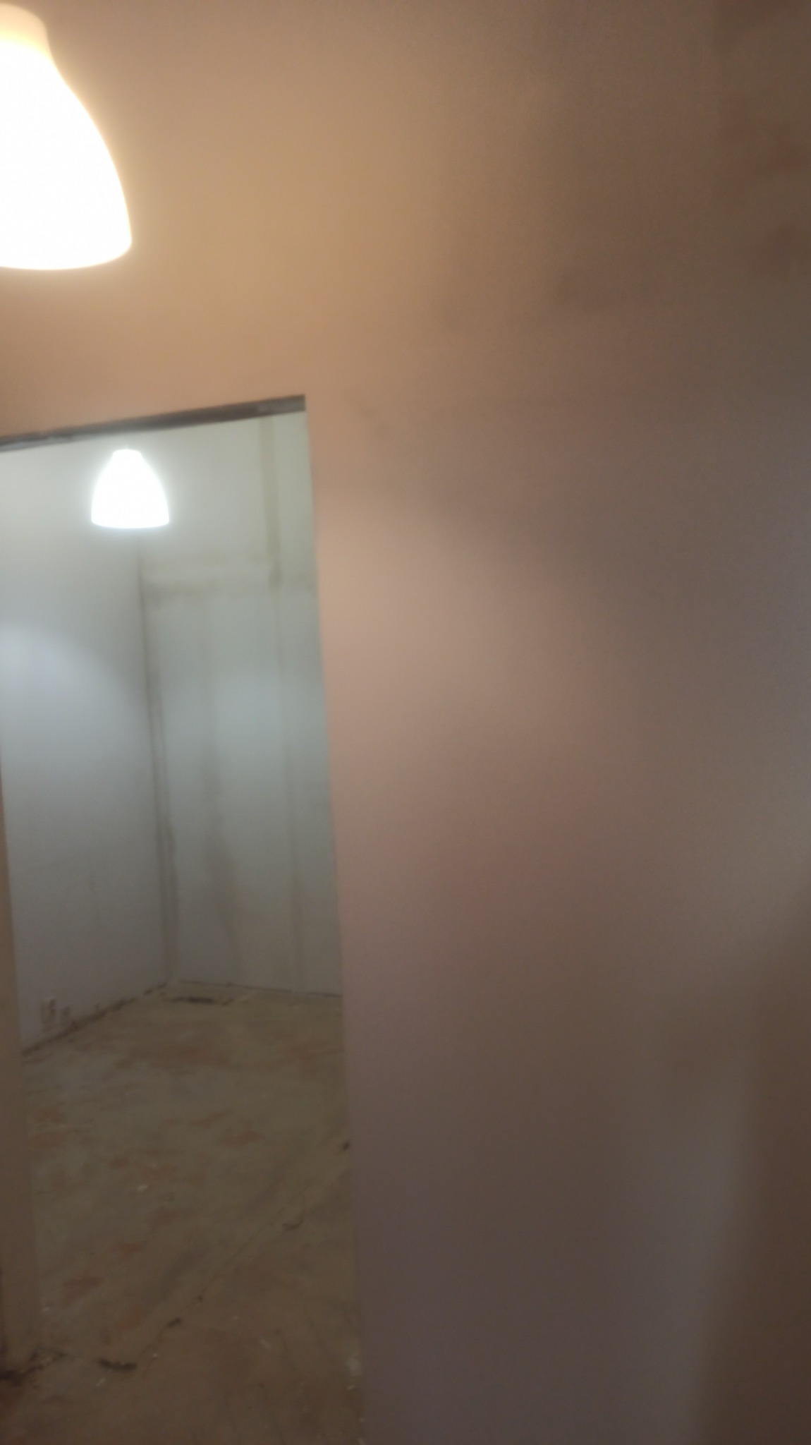 Pomieszczenie w trakcie prac, widoczne ściany po gruntowaniu, przygotowane do malowania, z widocznymi śladami po wcześniejszych pracach na podłodze.