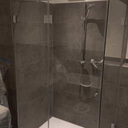 Alpeks.sp.zoo - Nowoczesna kabina prysznicowa z ciemnoszarymi płytkami, chromowanymi okuciami i białą brodzikiem, widok z zewnątrz, częściowo zakryta folią ochronną po instalacji.