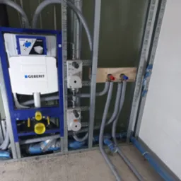 Stelaż podtynkowy Geberit Sigma zamontowany w konstrukcji szkieletowej, widoczne rury doprowadzające wodę z zaworami i izolowane rury kanalizacyjne, etap prac instalacyjnych.