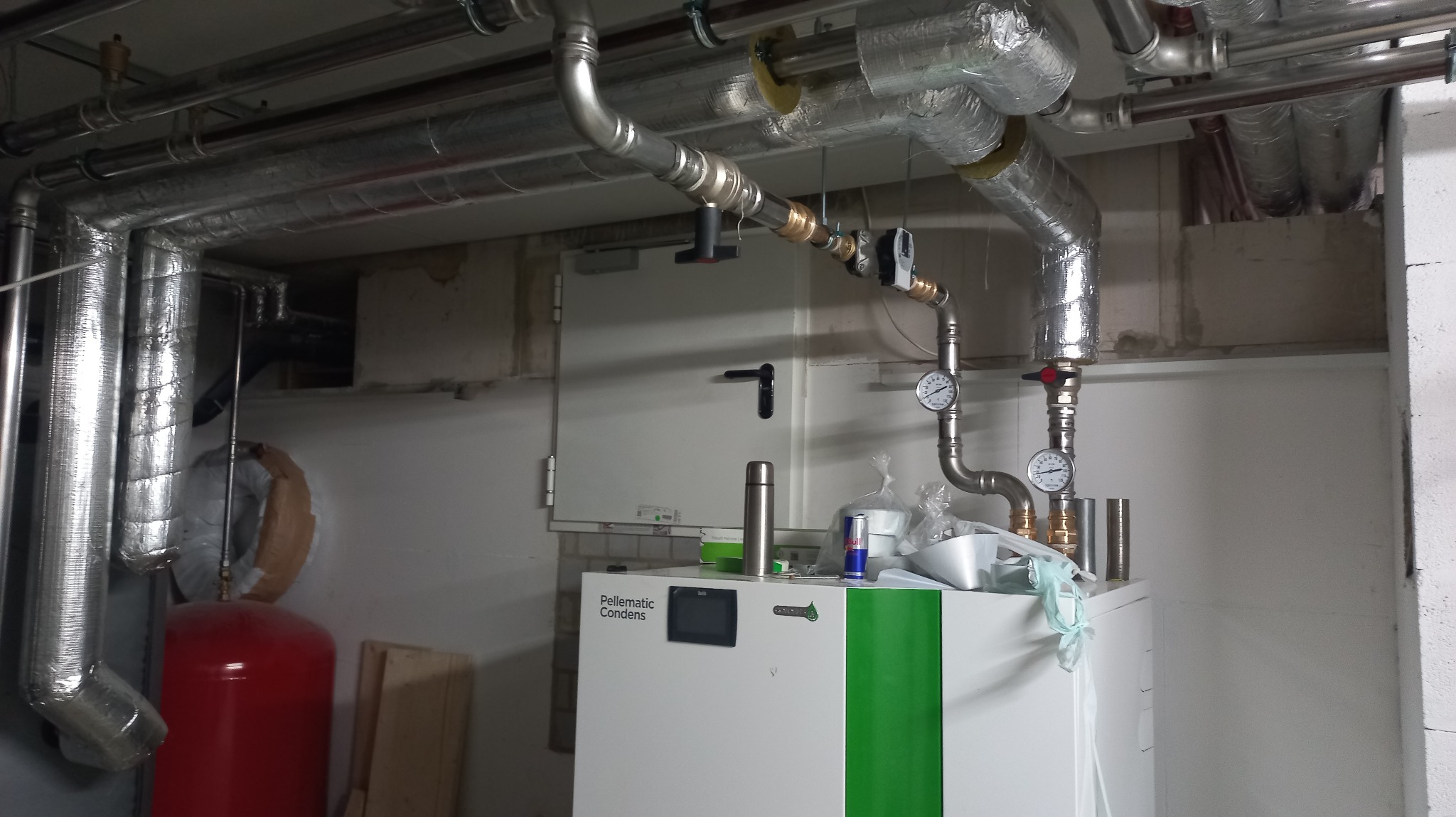 Komin wentylacyjny z rurami izolowanymi termicznie, manometry, zawory, ekspansomat w kotłowni z kotłem Pellematic Condens, widoczne elementy instalacji grzewczej.