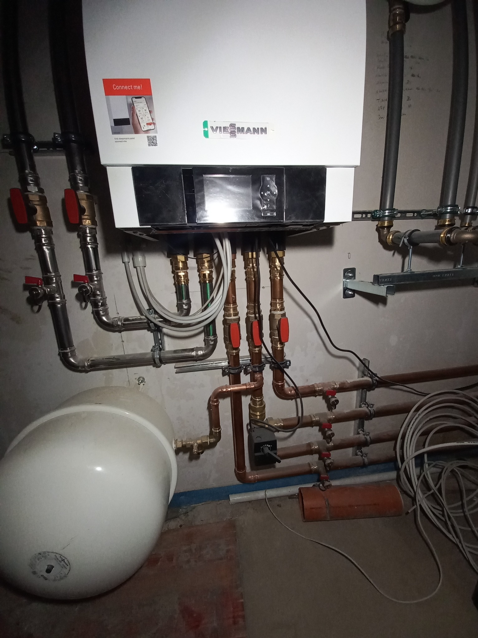 Zainstalowany wiszący piec gazowy Viessmann z podłączonymi rurami miedzianymi i stalowymi, widoczny zbiornik wyrównawczy, instalacja w trakcie podłączania, ściana z widocznymi śladami po pracach...