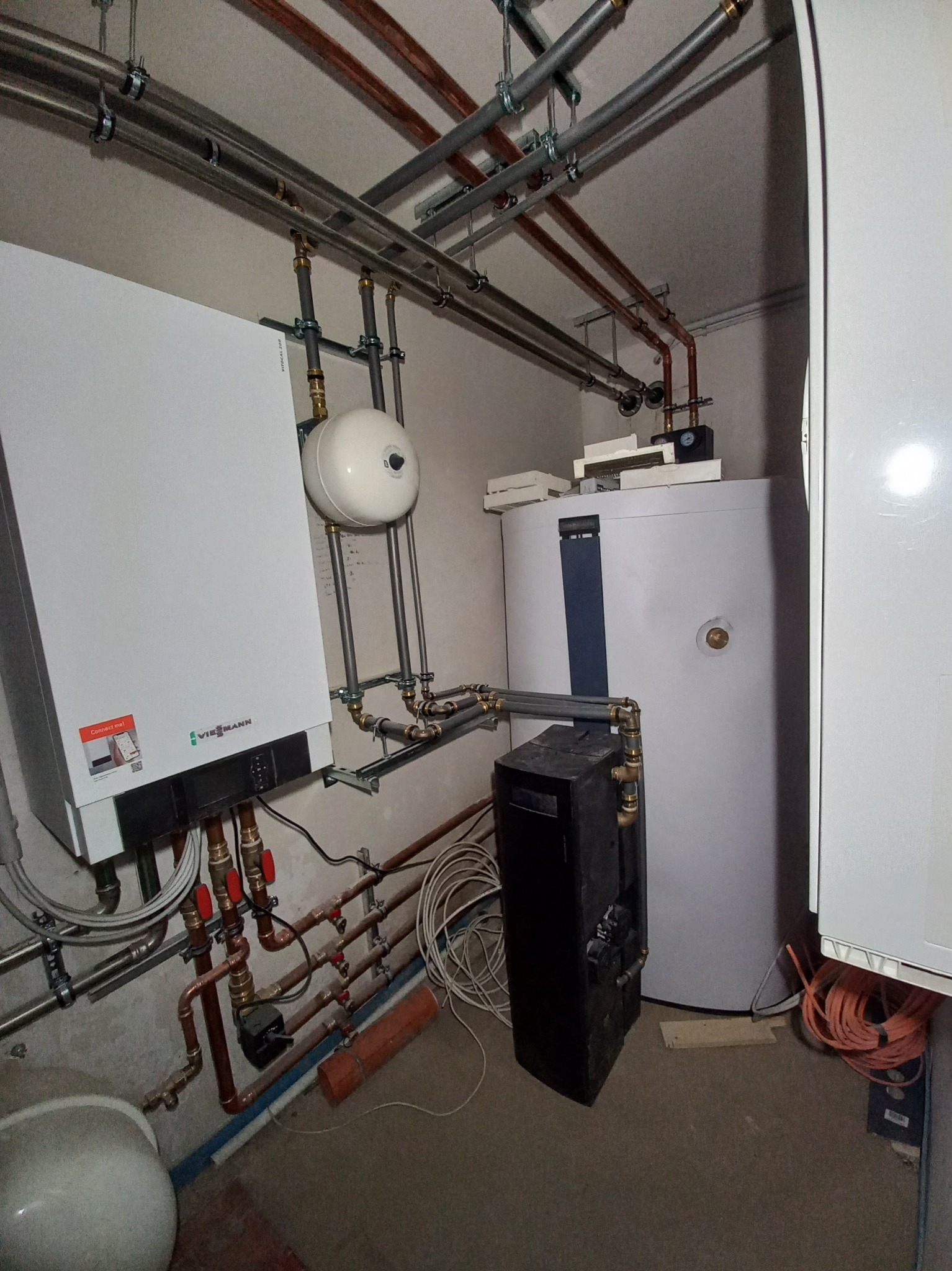 Nowoczesny piec gazowy Viessmann z podłączonym zasobnikiem ciepłej wody i instalacją hydrauliczną z rur miedzianych, widoczne elementy montażowe i osprzęt.