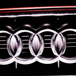 Daniel Smoter - Chromowane logo Audi na czarnym tle grilla samochodowego z subtelnym czerwonym akcentem na górze.