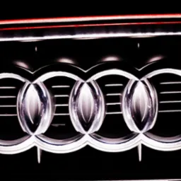 Chromowane logo Audi na czarnym tle grilla samochodowego z subtelnym czerwonym akcentem na górze.