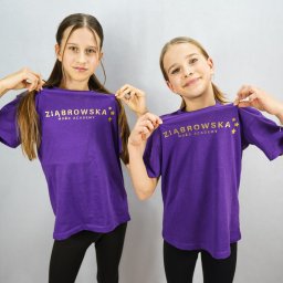 Daniel Smoter - Dwie uśmiechnięte dziewczynki w fioletowych koszulkach z logo 'Żiąbrowska Może Academy' na tle studyjnym.
