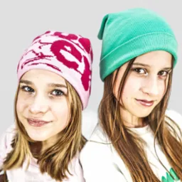 Portret dwóch nastolatek w kolorowych czapkach beanie: jedna w różowej z białym wzorem, druga w zielonej, stojących blisko siebie na jasnoszarym tle.