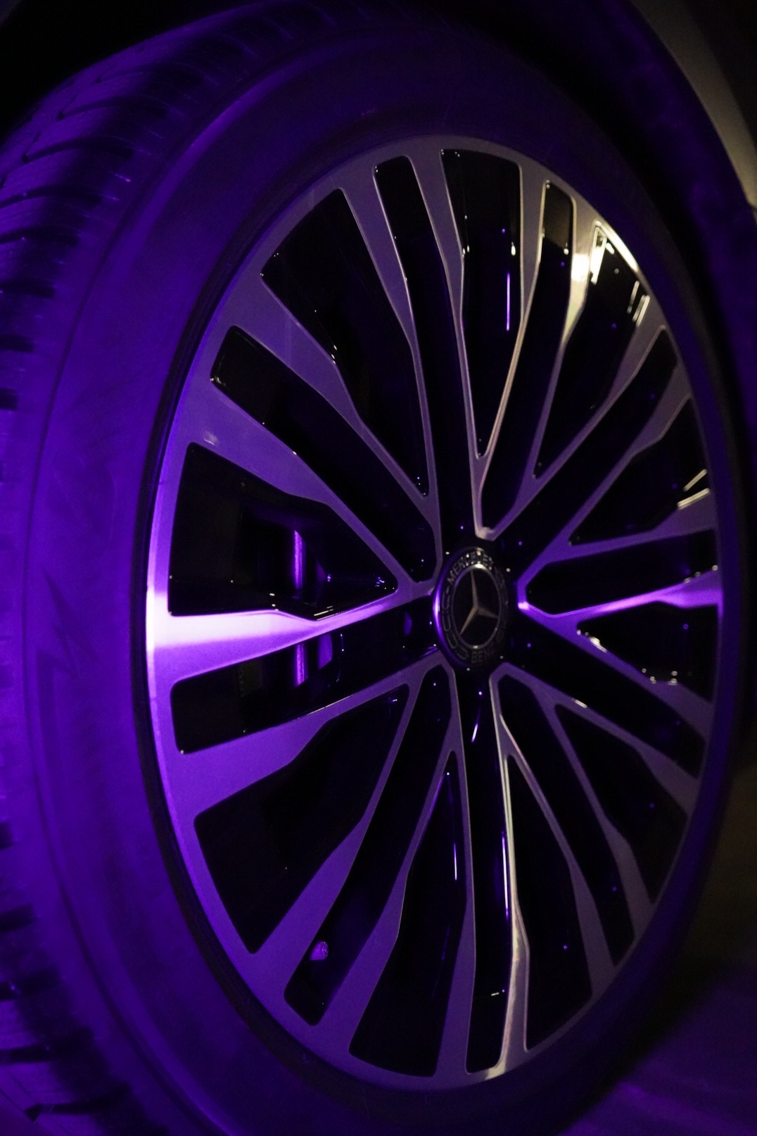 Felga aluminiowa Mercedes-Benz z oponą, oświetlona fioletowym światłem, widoczne logo producenta na deklu.