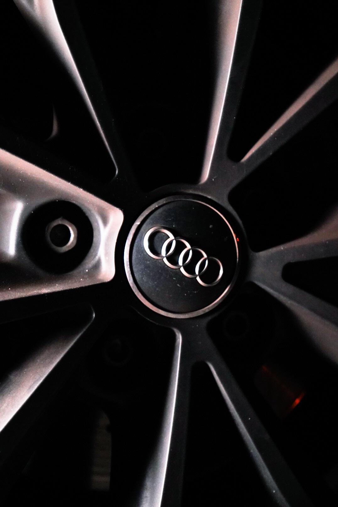 Ciemne, aluminiowe felgi samochodu Audi z widocznym logo producenta na czarnym tle w centrum koła.