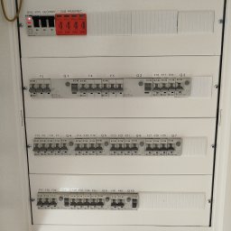 AD MIKOMAX Sp.z o.o. - Rozdzielnica elektryczna z wyłącznikami różnicowoprądowymi i zabezpieczeniami przepięciowymi, widoczne oznaczenia obwodów i tabliczka z numerem telefonu