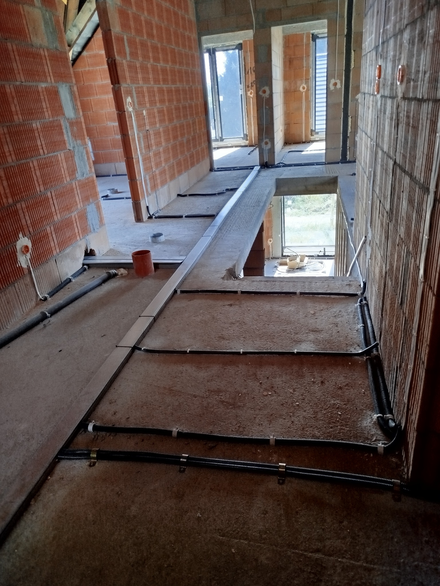 Surowy stan budynku w trakcie prac instalacyjnych: widoczne kable elektryczne prowadzone po podłodze i ścianach z pustaków ceramicznych, przygotowane punkty przyłączeniowe, brak wykończenia.