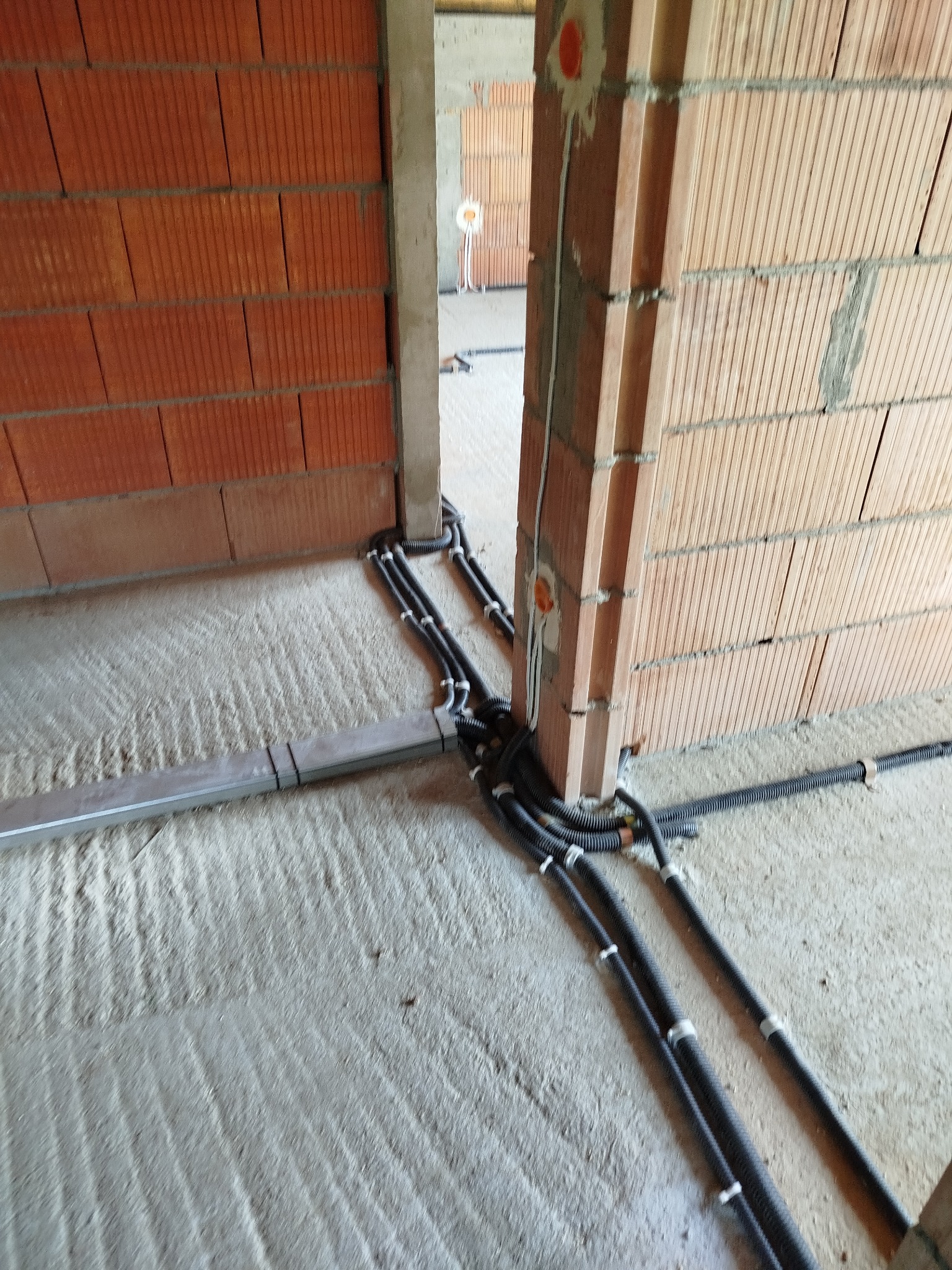 Wewnętrzne okablowanie elektryczne w peszlach, prowadzone wzdłuż ścian z pustaków ceramicznych w surowym stanie, widoczne pomarańczowe puszki instalacyjne.