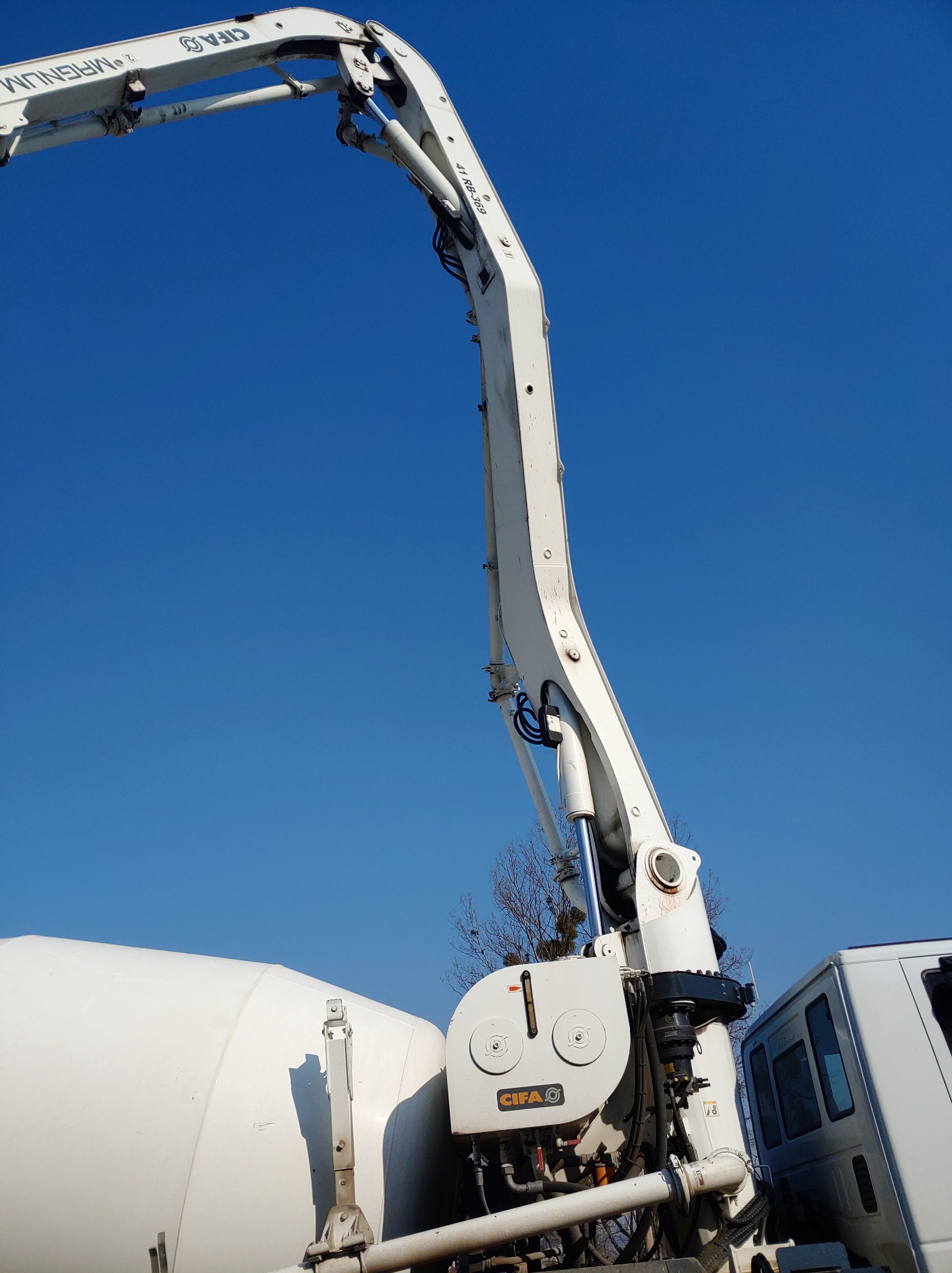 Widok z dołu na biały wysięgnik pompy do betonu marki CIFA na tle błękitnego nieba.