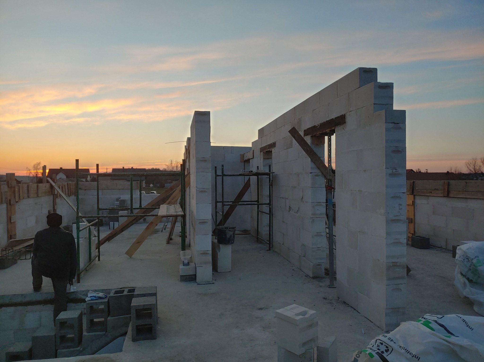 Wznoszone ściany domu z betonu komórkowego Ytong w trakcie budowy, widoczne rusztowania i zaprawa, w tle zachodzące słońce.
