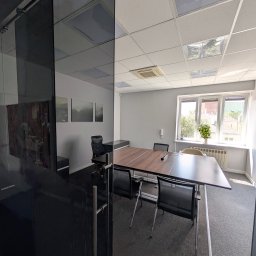 BRIGHTHOUSE SPÓŁKA Z OGRANICZONĄ ODPOWIEDZIALNOŚCIĄ - Nowoczesna sala konferencyjna z dużym stołem i krzesłami, widoczna przez szklane drzwi. Minimalistyczny wystrój, jasne ściany i dywan w neutralnym kolorze.