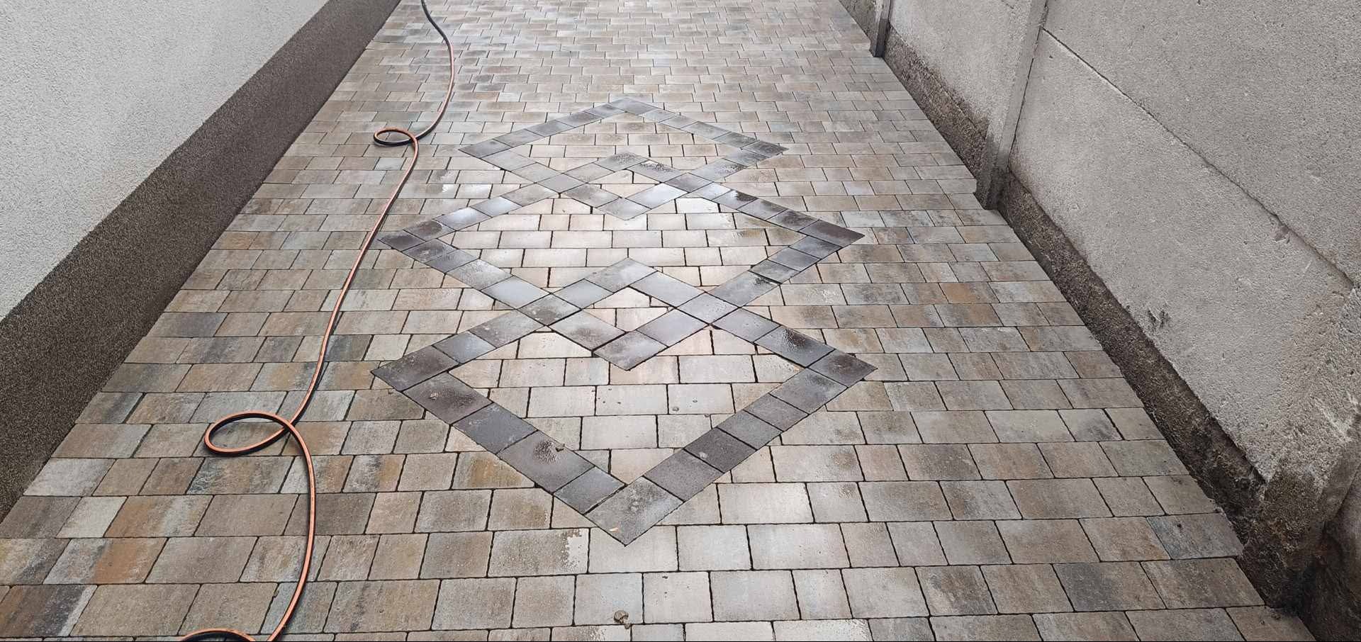 Ułożona kostka brukowa tworząca wzór na podwórku. Widoczny przewód. Estetyczne wykończenie przestrzeni zewnętrznej.